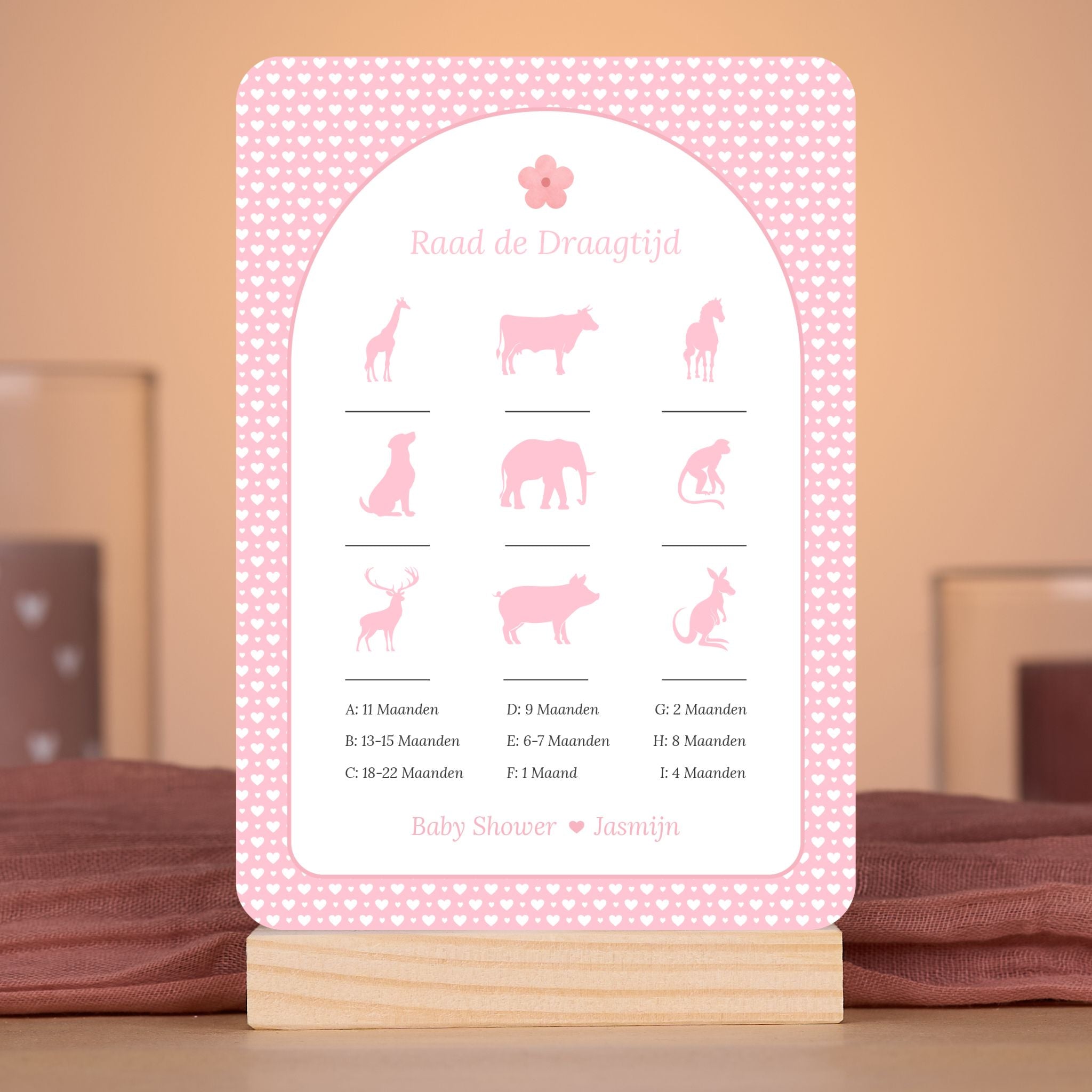 Raad de Draagtijd kaart met witte hartjes op roze achtergrond en bloemaccent – sfeervolle setting met babyshower decoratie – Studio Miron